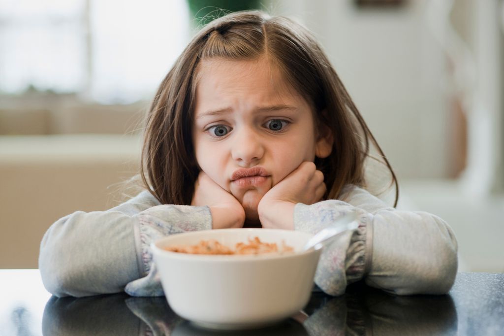 Niña pequeña con cara de rechazo ante un bol de comida