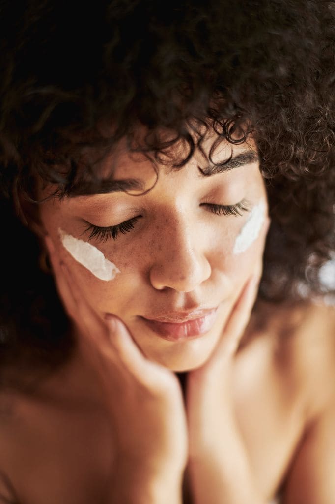 Rostro de mujer con los ojos cerrados y crema en las mejillas