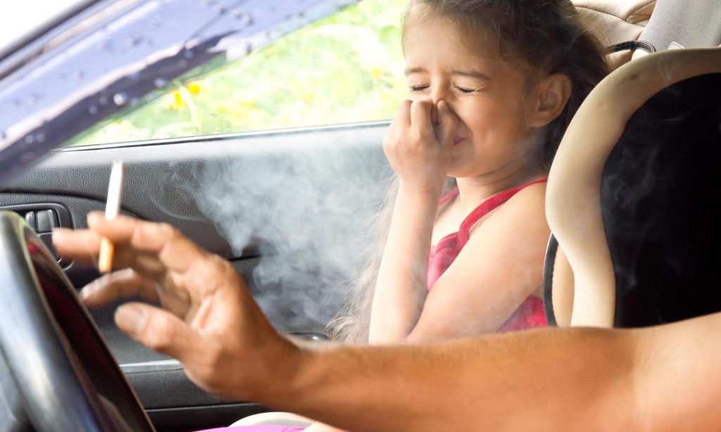 padre fumando delante de su hija dentro del coche