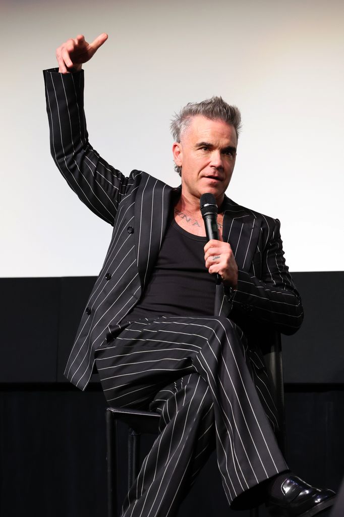 Plano medio de Robbie Williams en una entrevista con traje negro de rayas
