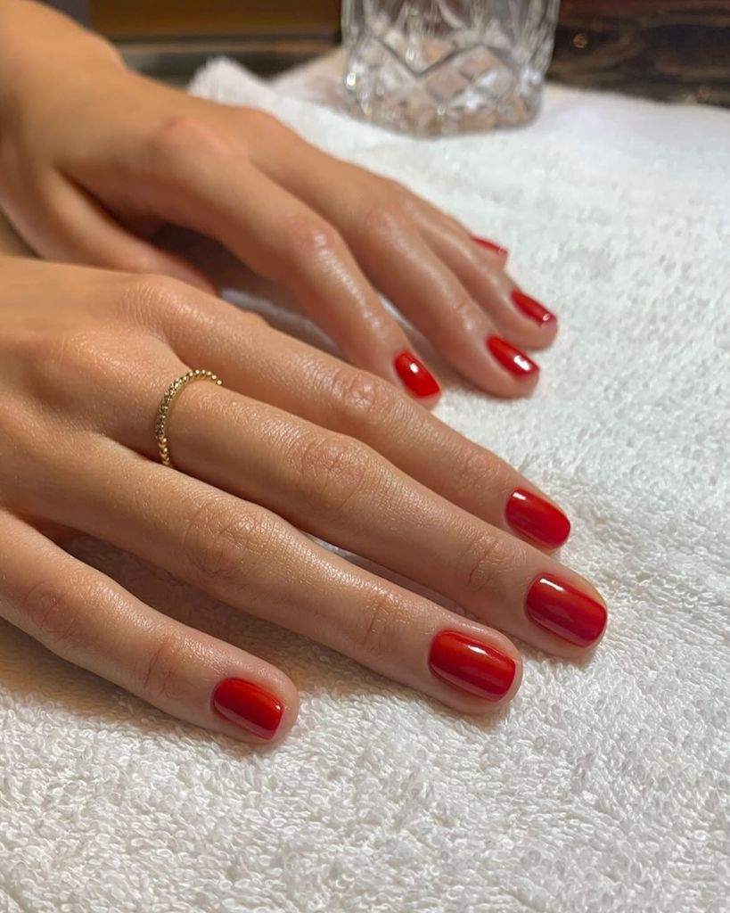 Manos con manicura roja sobre una mesa con vaso de cristal de fondo