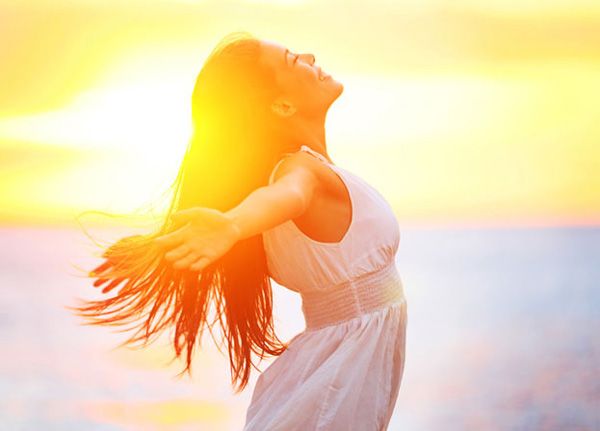 Mujer con cabello largo y vestido blanco, brazos extendidos al atardecer.