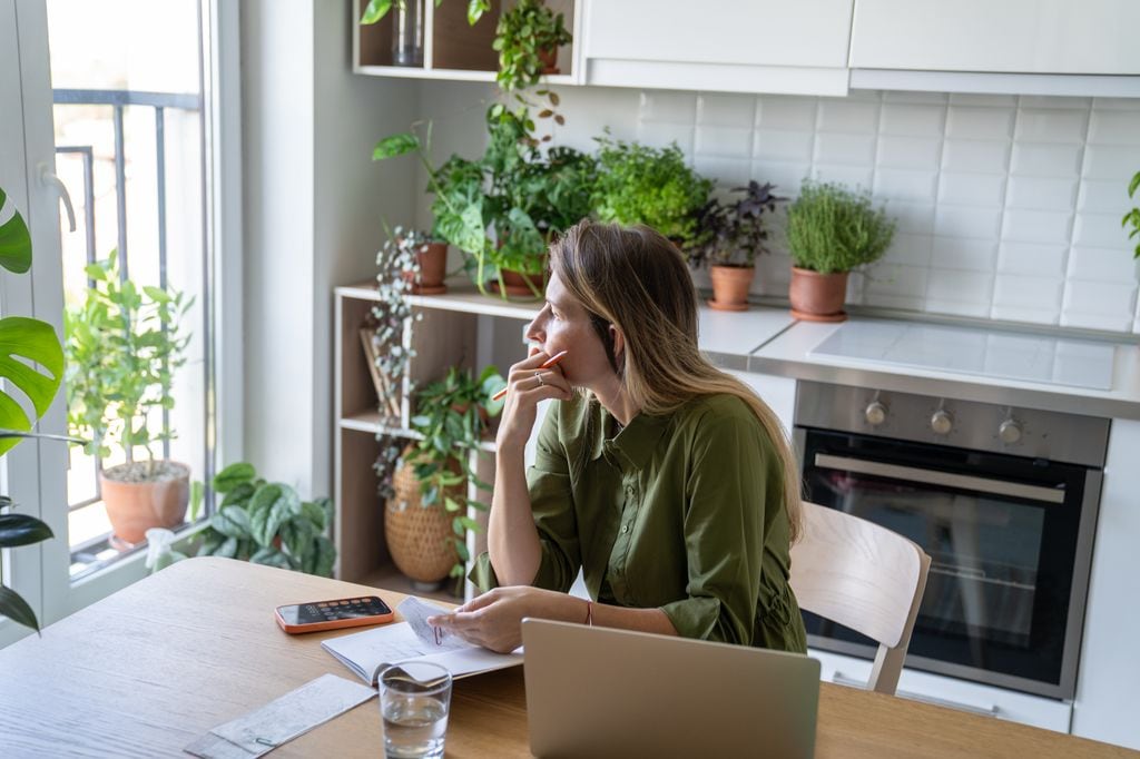 mujer preocupada en la cocina de su casa, revisando facturas