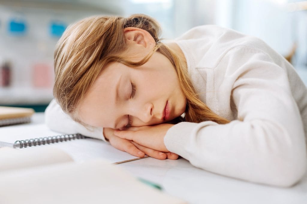 Niña con narcolepsia dormida sobre la mesa de estudio