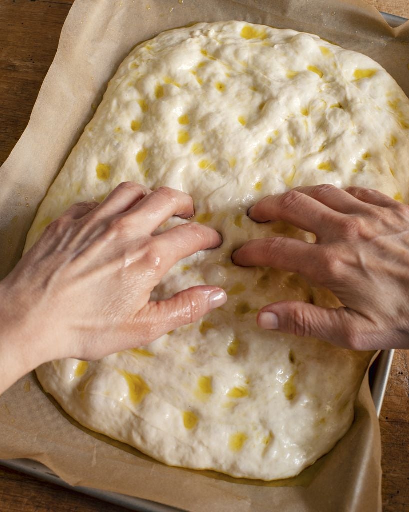 Haz hoyuelos profundos en la masa con los dedos y pon un chorrito de aceite en cada uno. Esto crea pequeños “pozos” perfectos para que los toppings se impregnen y la focaccia quede jugosa y sabrosa por dentro.