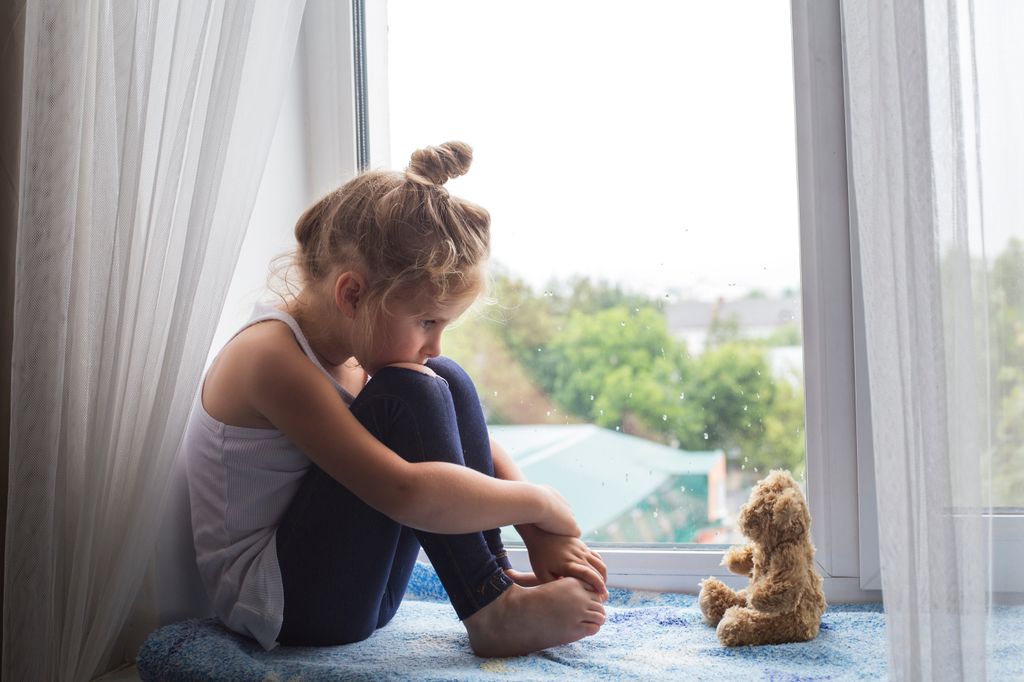 Niña triste víctima de acoso sentada en la ventana