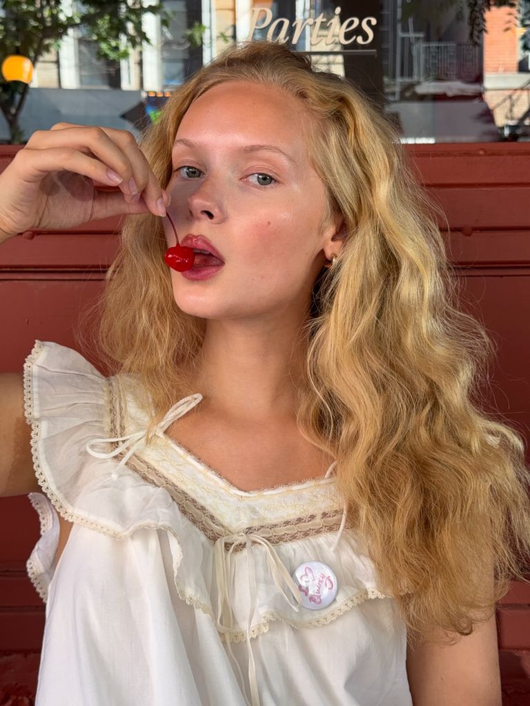Mujer rubia con el pelo ondulado comiendo una cereza