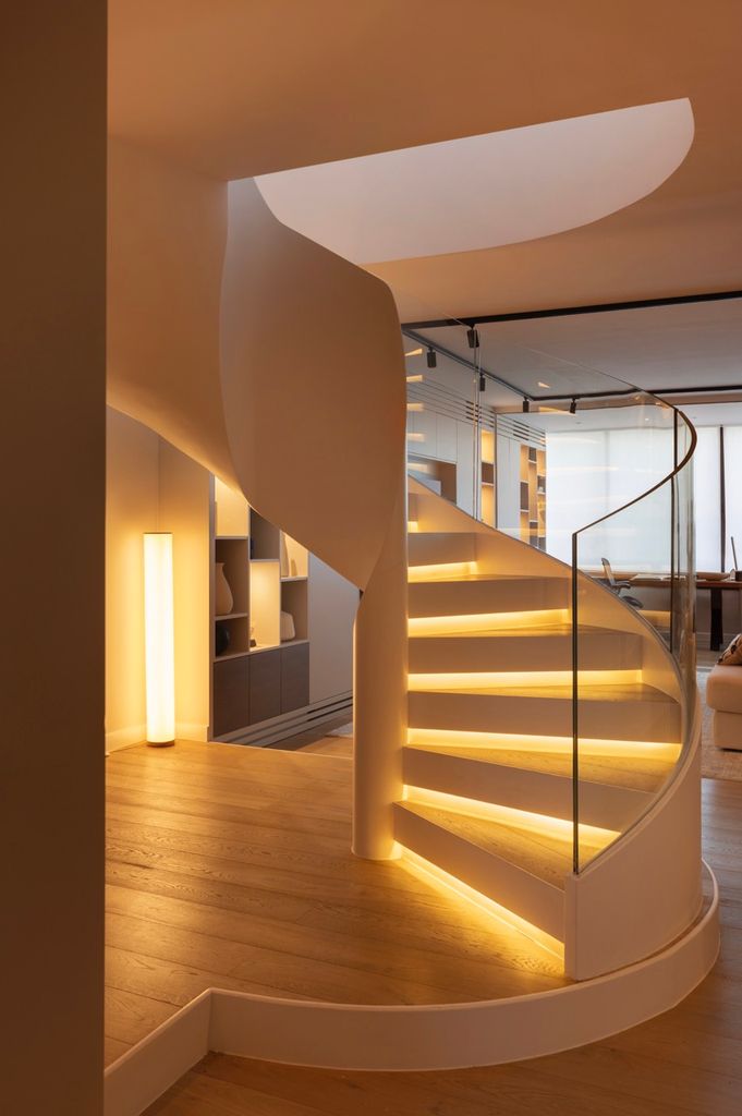 Escalera de formas sinuosas con una buena iluminación en cada peldaño y barandilla transparente