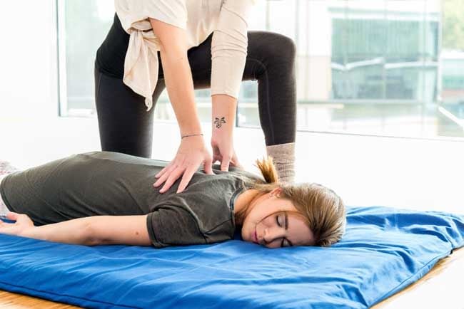 Mujer tumbada sobre una colchoneta recibiendo un masaje de shiatsu