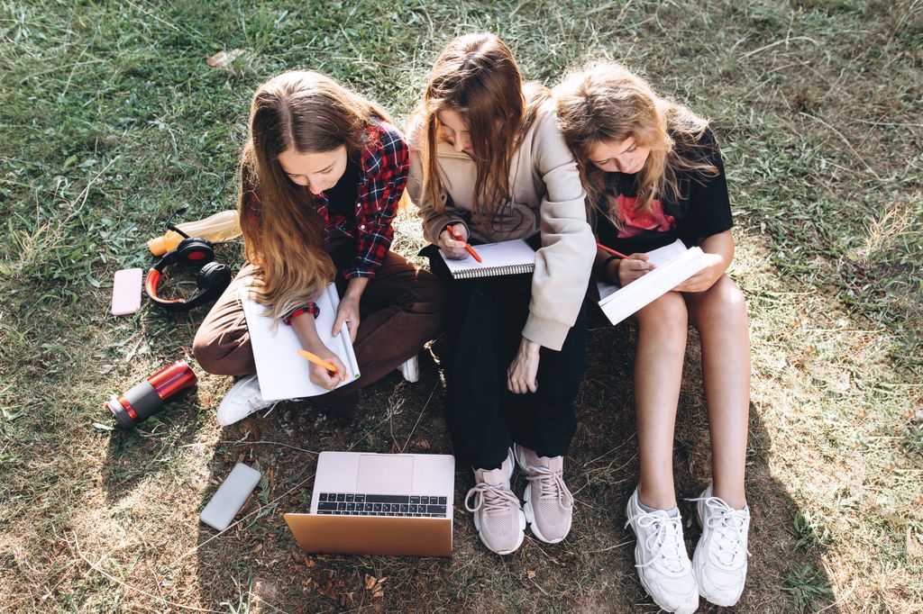 grupo de adolescentes haciendo los deberes juntas sentadas en el césped