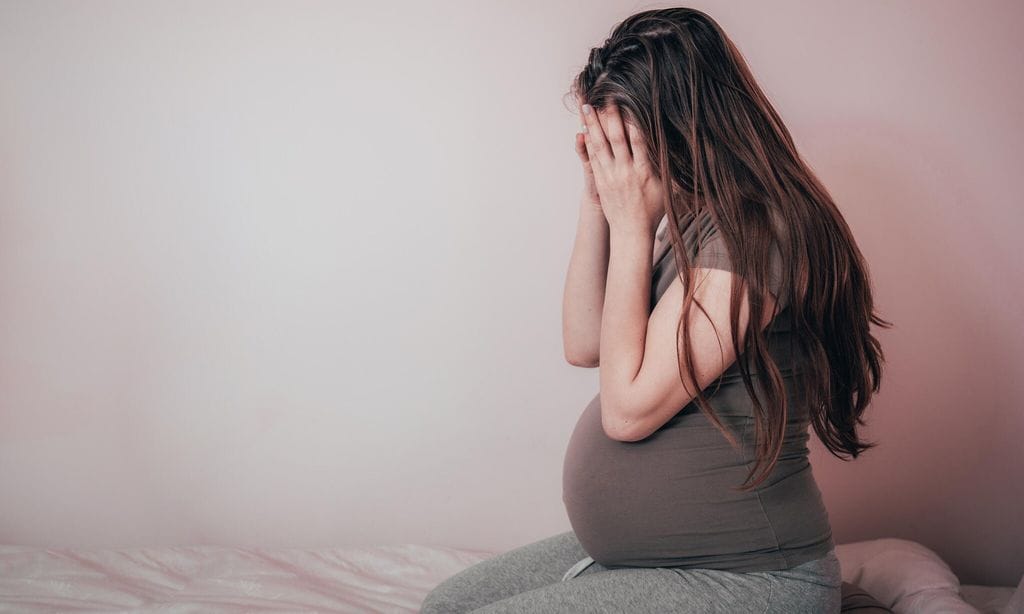 embarazada triste tap ndose la cara con las manos sobre la cama