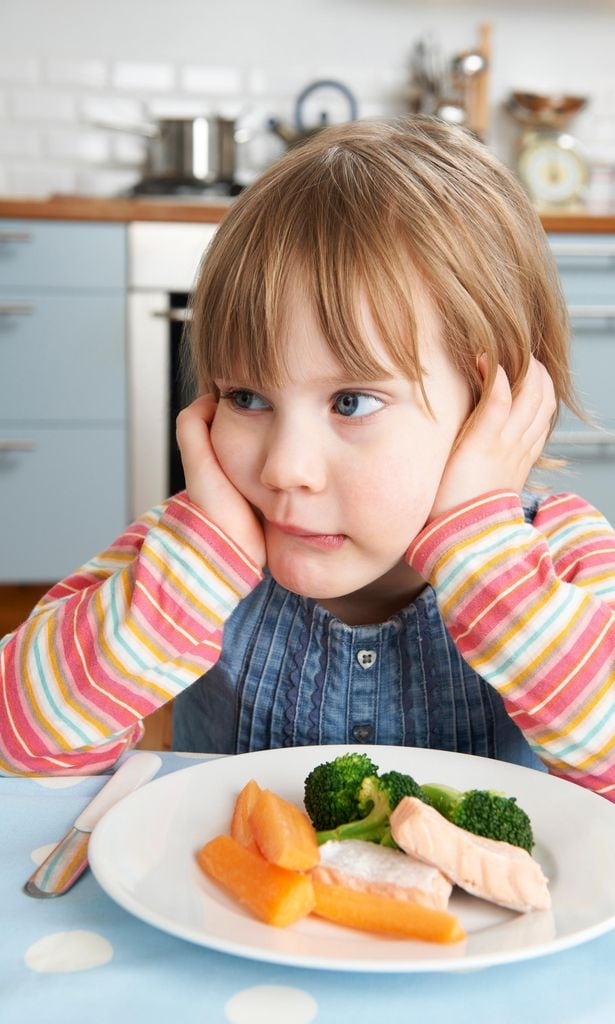 Niña no quiere comer sentada en la mesa con plato de comida delante
