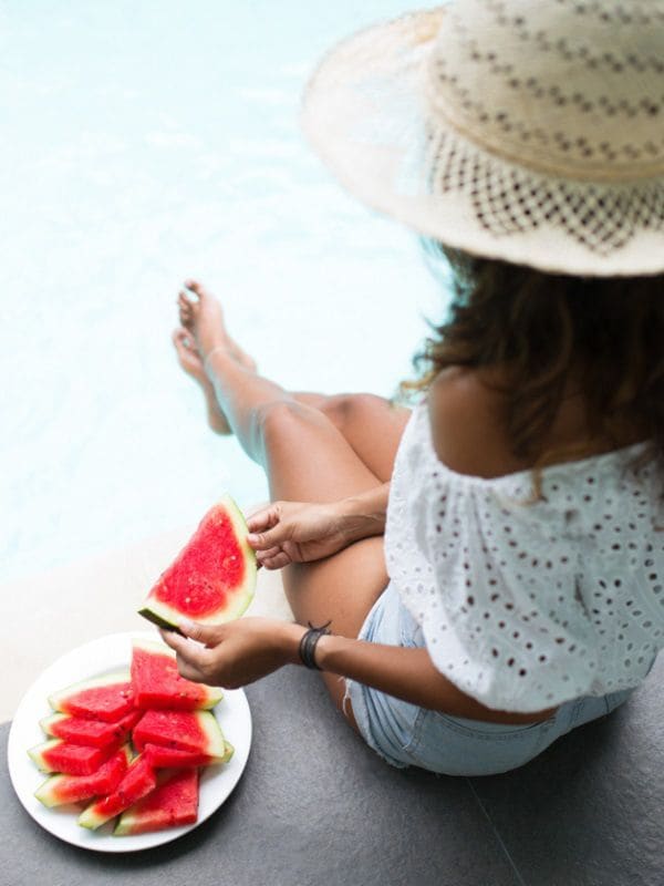 Mujer come sandía al borde de la piscina