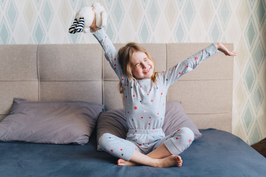 Niña recién despierta estirándose en la cama