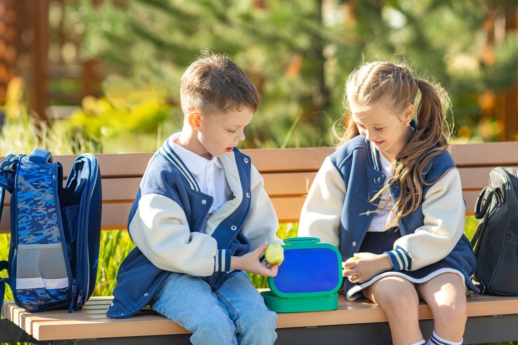 niños en un banco abriendo su merienda en el recreo