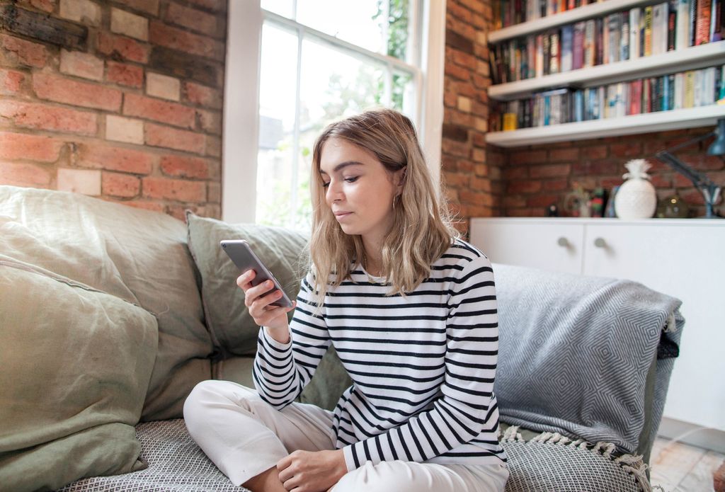 mujer sentada en el sofá, con gesto serio, mirando su móvil