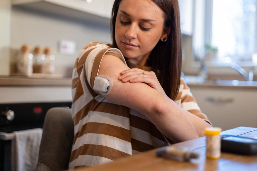 mujer con diabetes mirándose su sensor de glucosa en el brazo