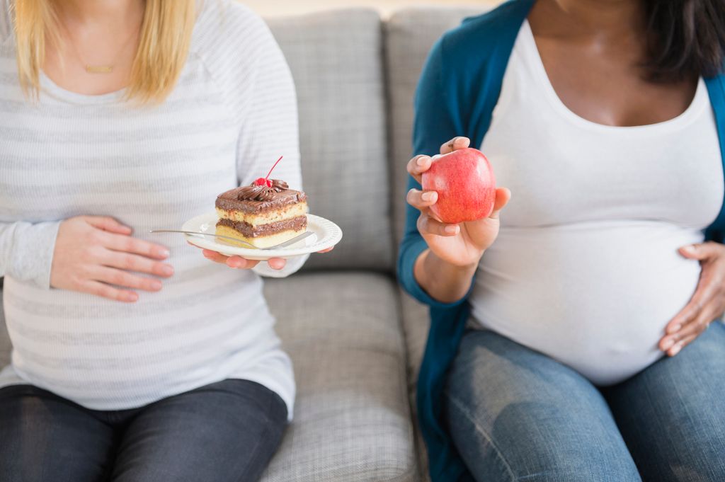 Embarazadas juntas, una con una manzana y otra con un trozo de pastel