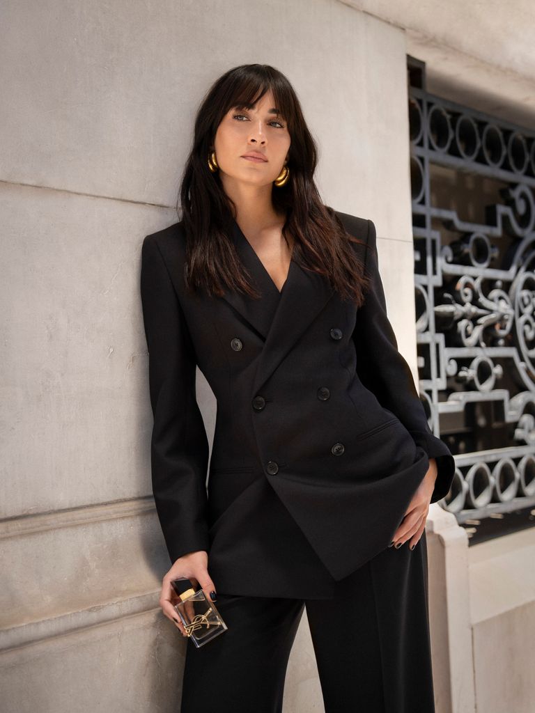 Aitana con traje de chaqueta negro, el pelo suelto y accesorios dorados en la calle