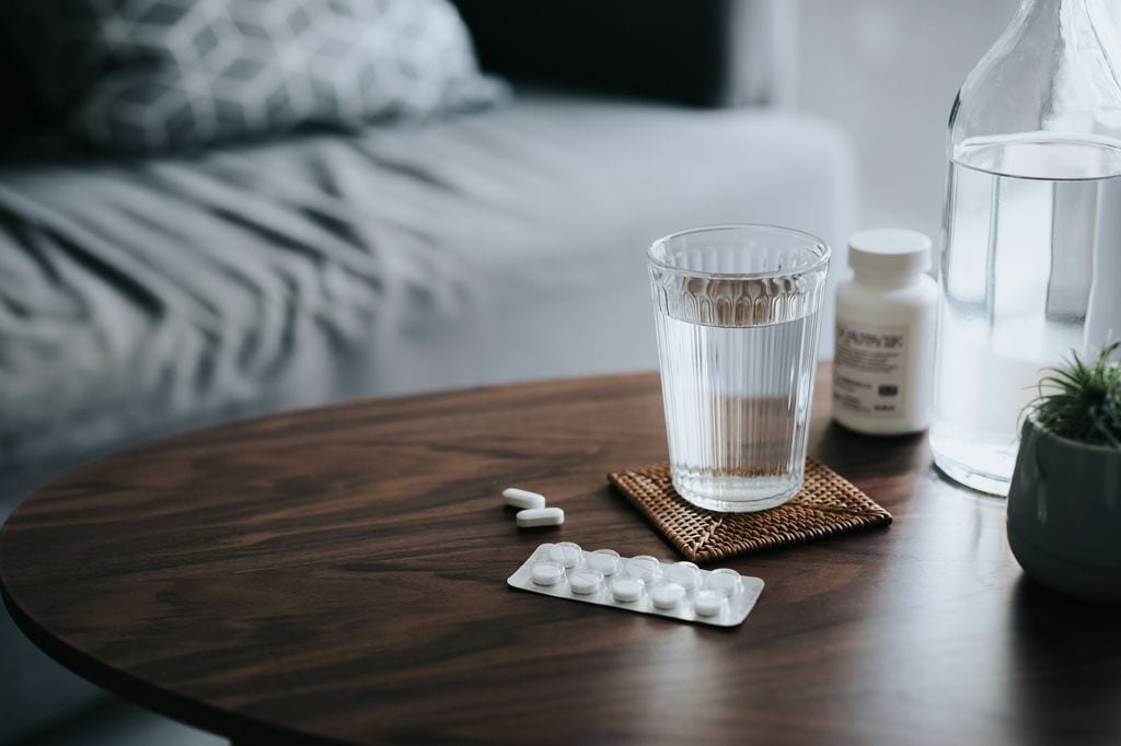 pastillas y un vaso de agua en la mesilla junto a la cama