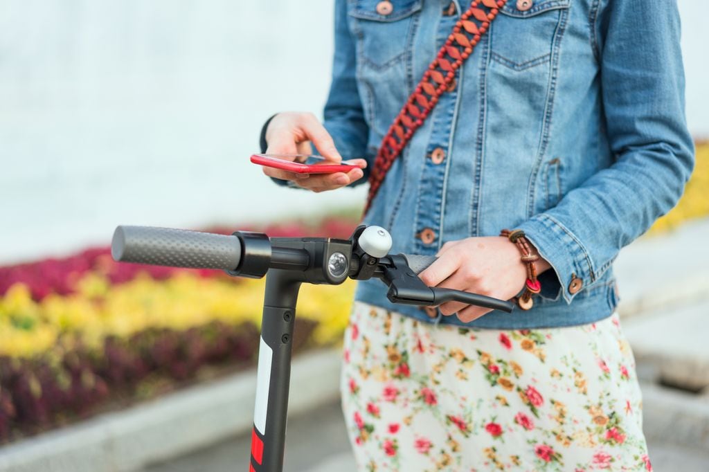 Una chica con su móvil junto a un patinete eléctrico