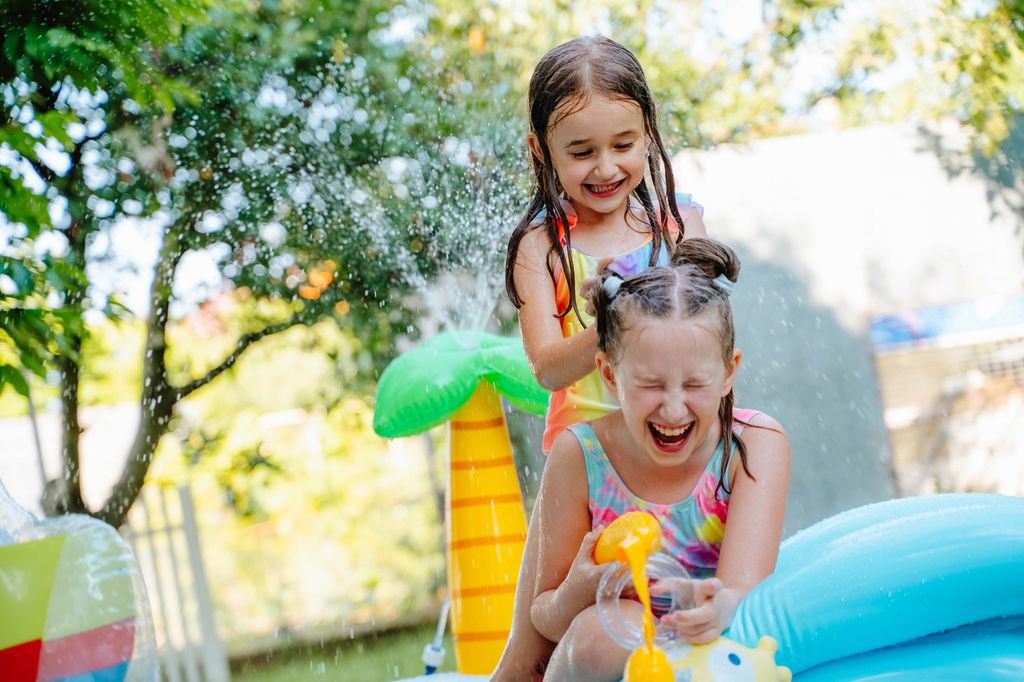 dos niñas jugando con el agua en el jardín en verano