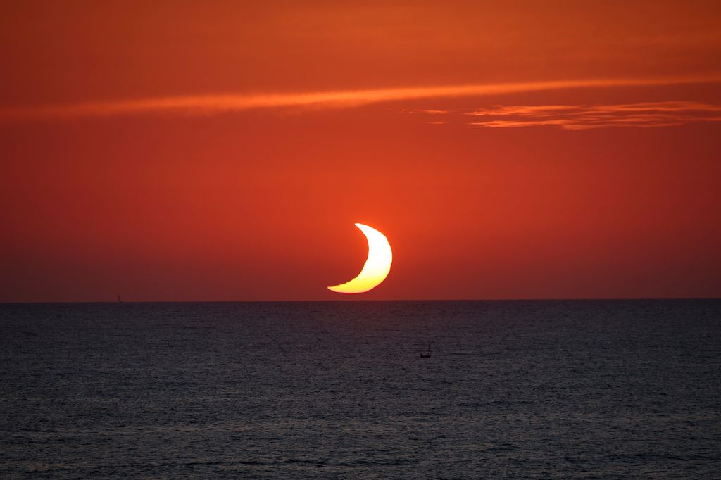 El eclipse transforma el atardecer en Port de Sóller, Mallorca, donde el Sol parcialmente oculto por la Luna parece hundirse en el Mediterráneo convertido en una brillante media luna.