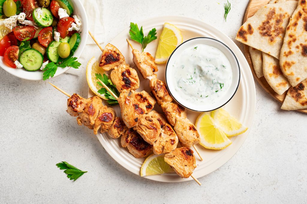 Brochetas de pollo con salsa tzatziki y ensalada.