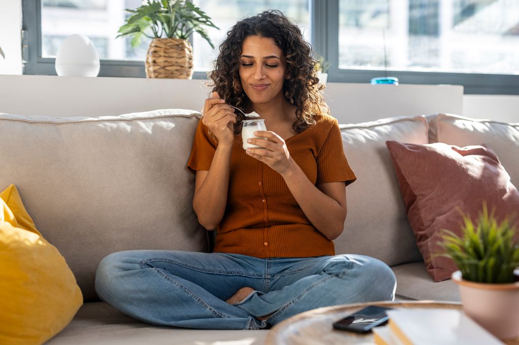 mujer comiendo un yogur sentada en el sofá