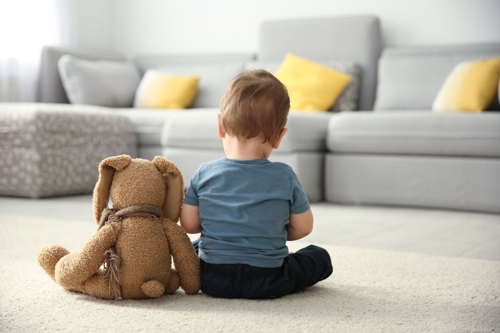 Un niño pequeño sentado de espaldas junto a su oso de peluche