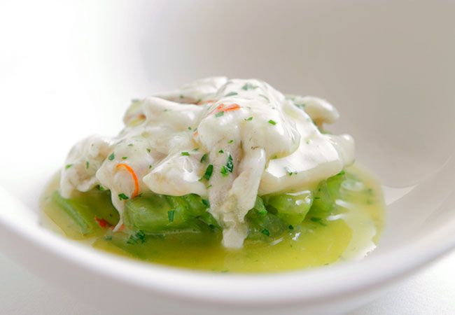 Plato de mariscos blancos y verdes en salsa, servido en un cuenco blanco.