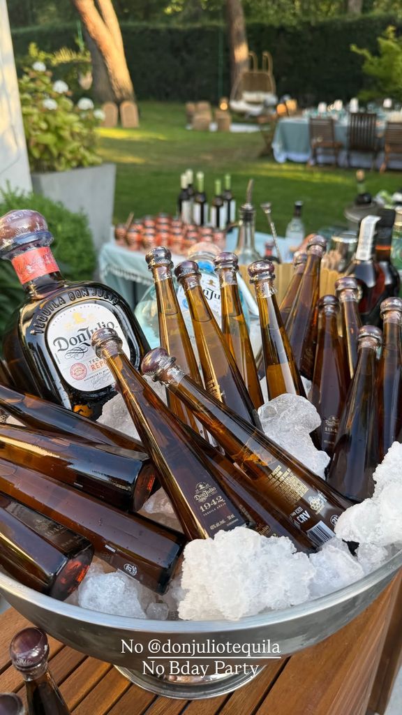 Recipiente metálico con hielo y botellas de tequila Don Julio en una fiesta al aire libre.