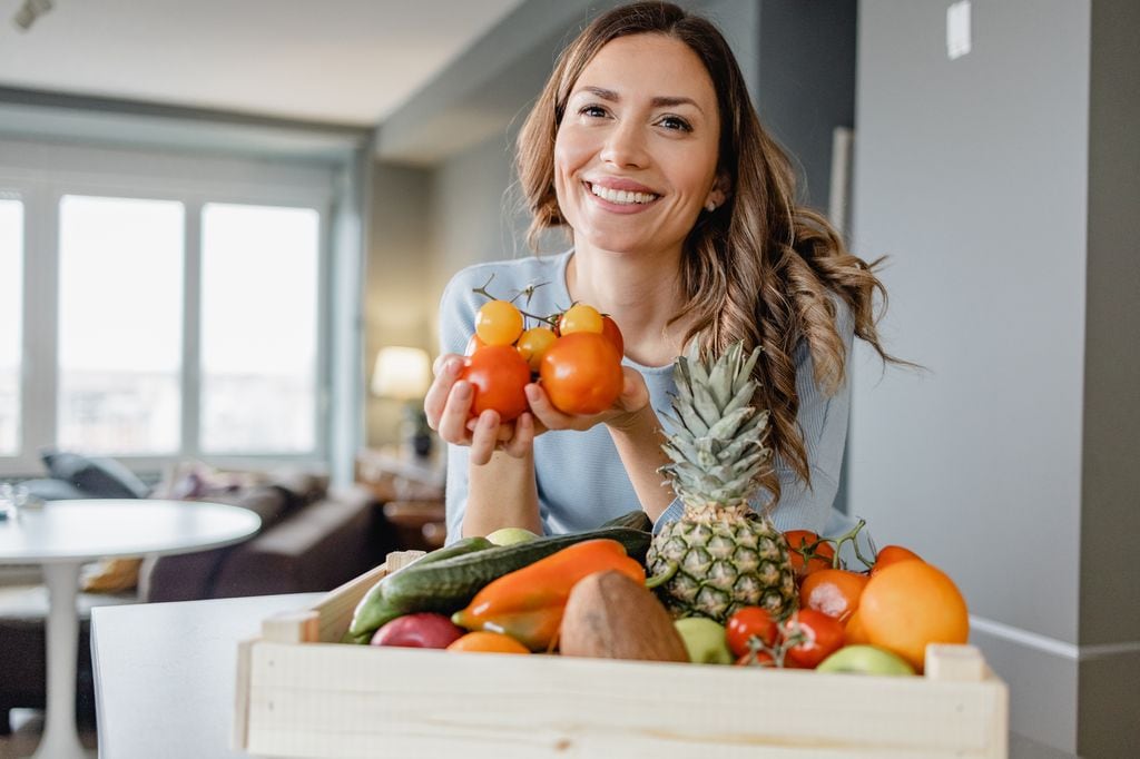 Mujer sonriendo con frutas y hortalizas en una cesta 