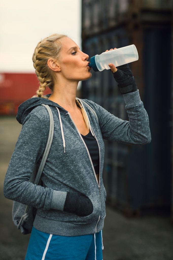 Mujer rubia con trenzas y chaqueta deportiva bebiendo agua de una botella