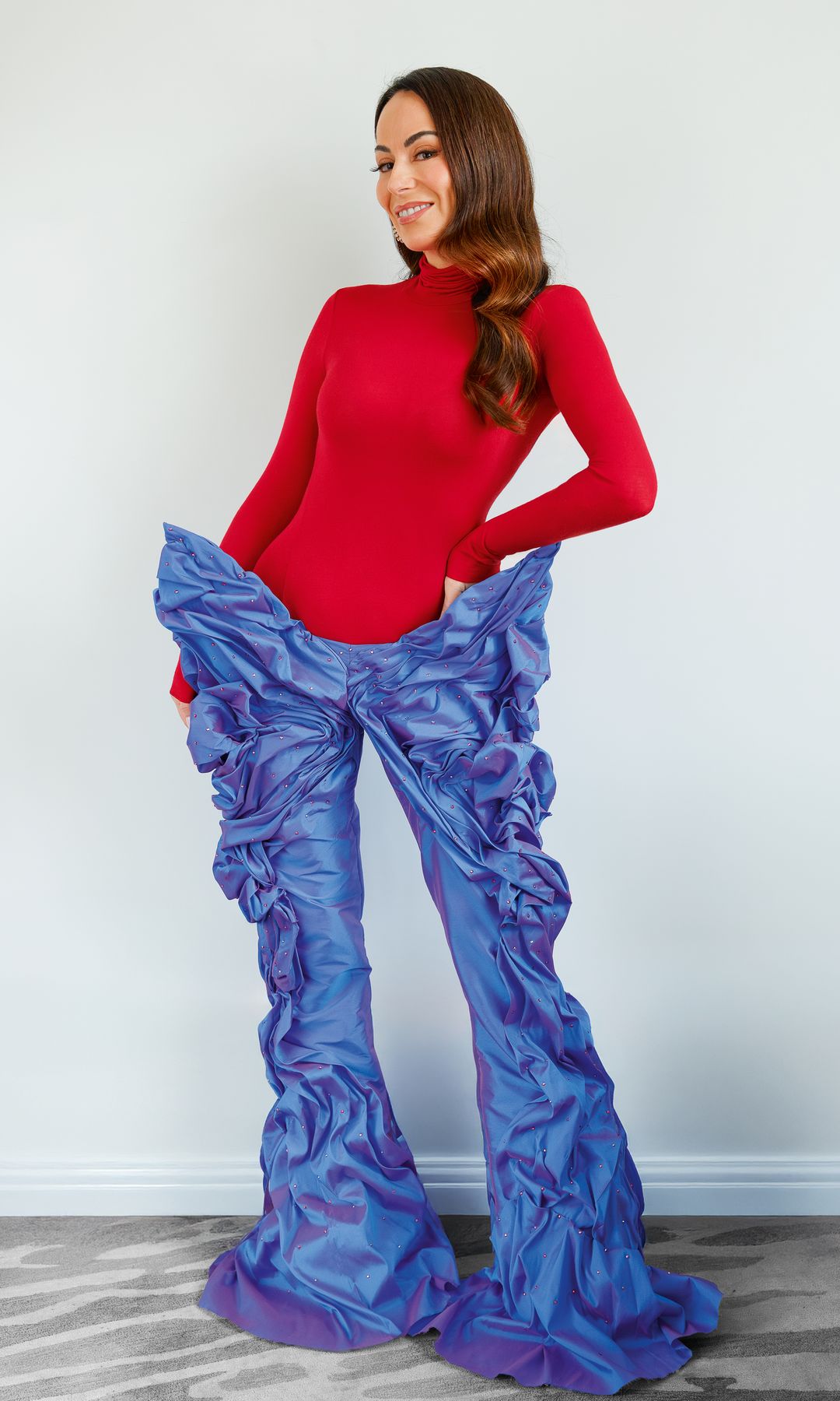 María Escoté con cabello largo, sonriendo, en ropa roja y pantalones azules con volantes.