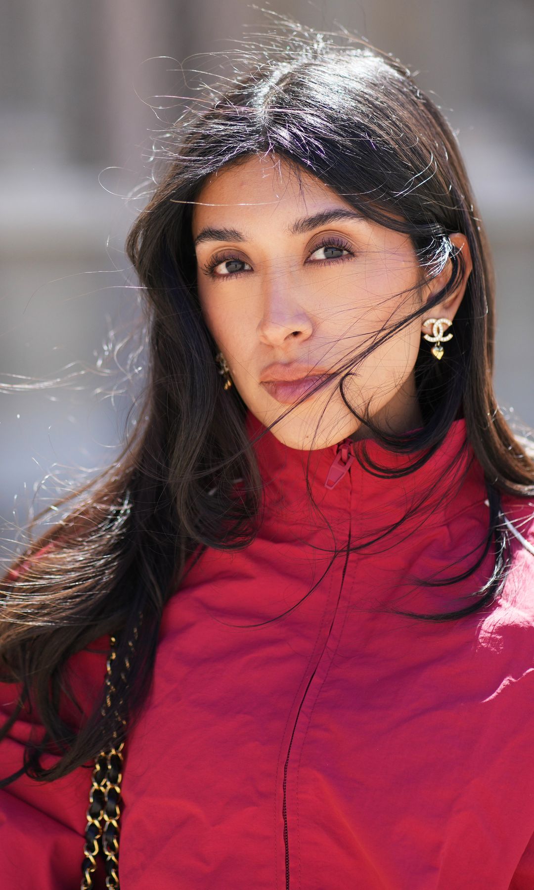 PARIS, FRANCE - APRIL 24: Angela Gonzalez wears long wavy dark brown hair, a red zip-front windbreaker jacket with white lines by Zara, Chanel earrings, during a street style fashion photo session, on April 24, 2026 in Paris, France