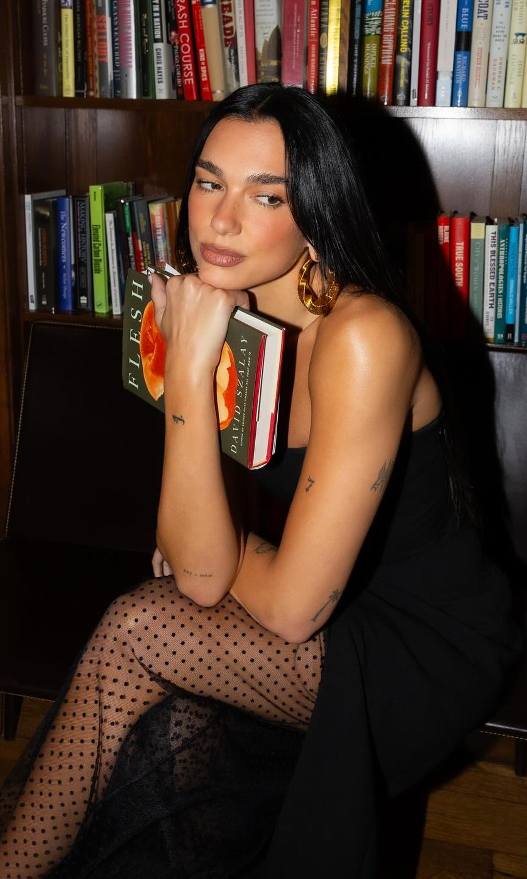 Dua Lipa frente a una librería sosteniendo un libro en sus manos