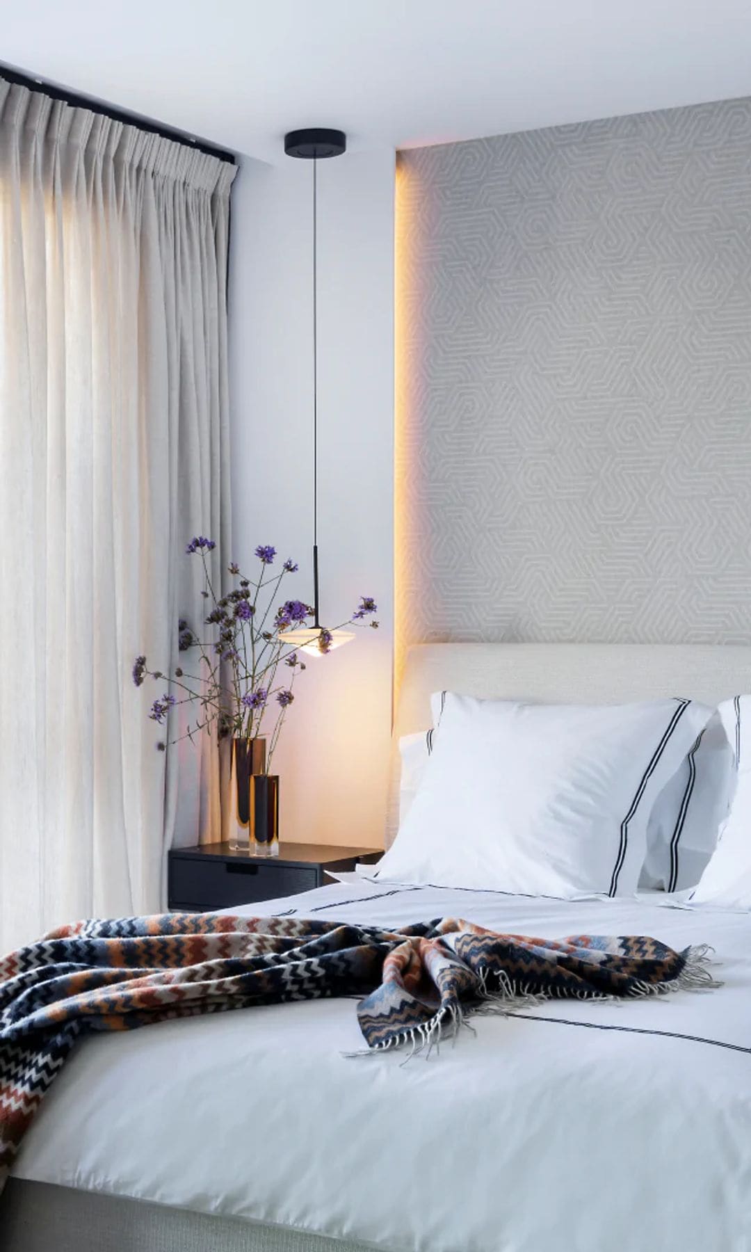 Dormitorio con salida a la terraza, ropa de cama blanca, cortinas blancas, jarrones en la mesita de noche, iluminación en la pared, aplique de pared sobre la mesita de noche, manta de colores sobre la cama