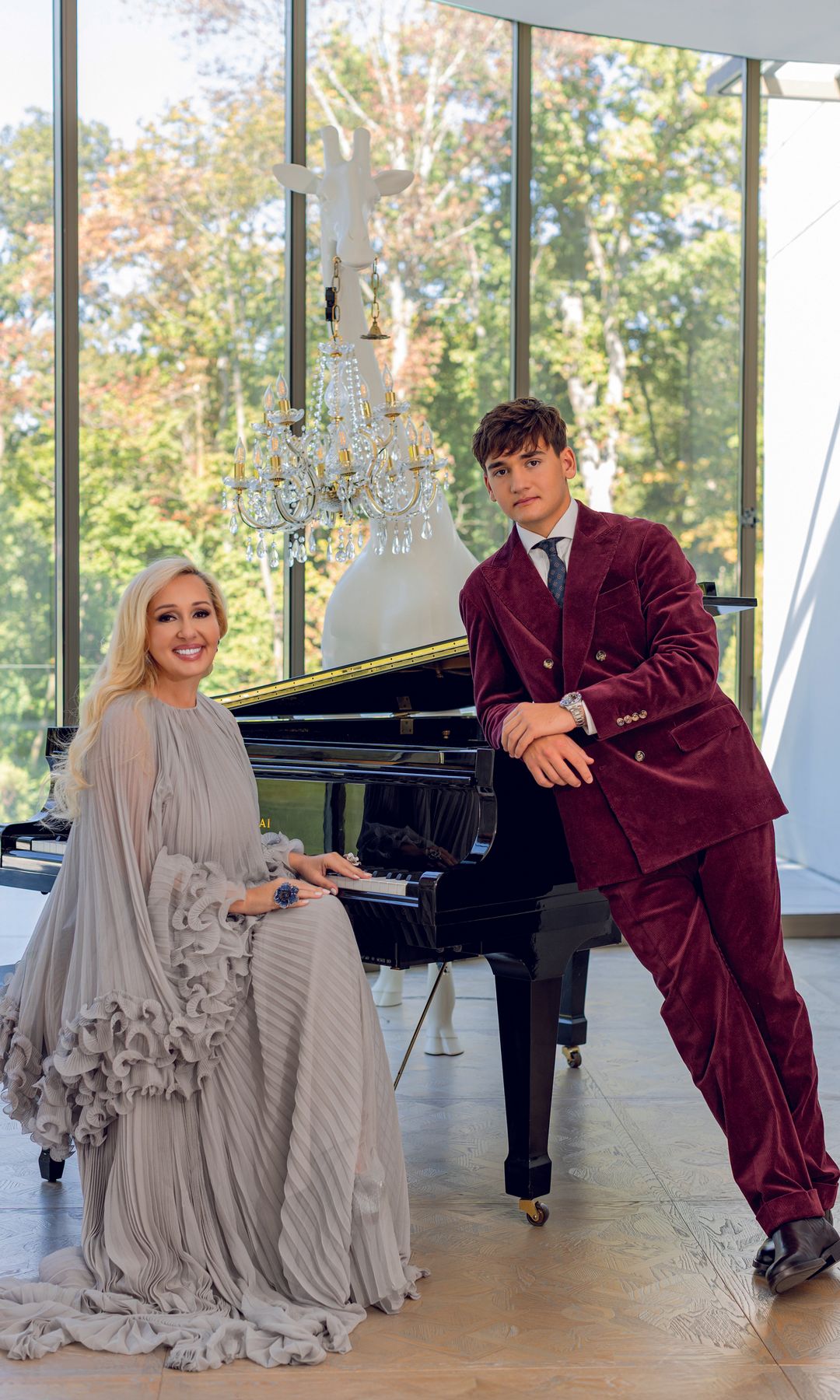 Monique Delacroix en vestido gris y hombre en traje rojo junto a un piano.