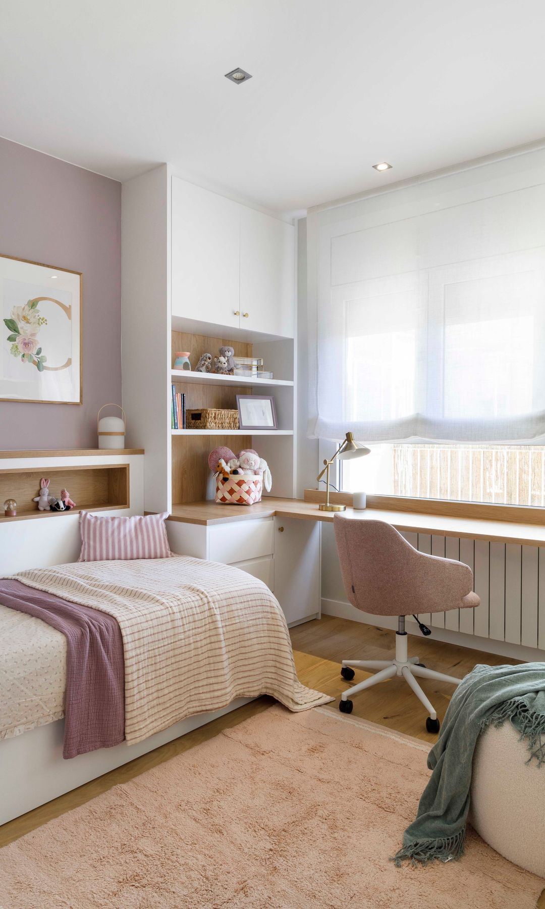 Habitación infantil con escritorio bajo la ventana con radiador, estor blanco, mueble a medida con estantería