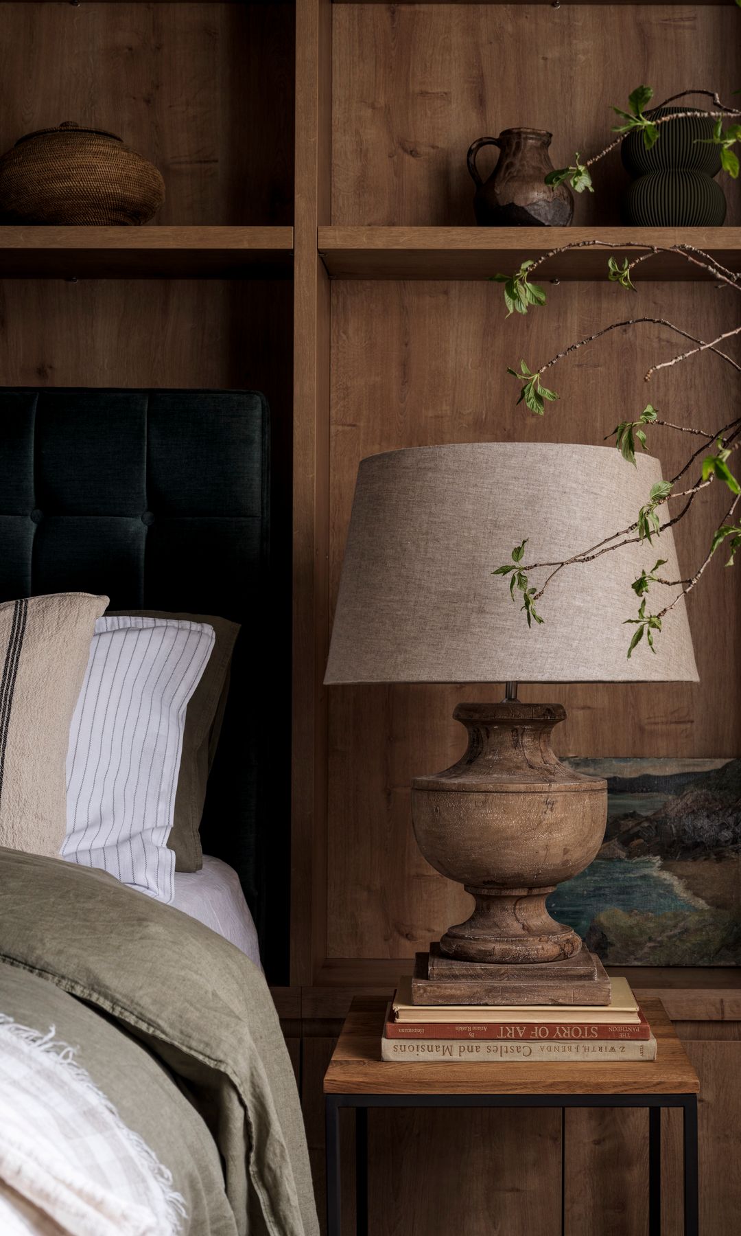 Dormitorio con pared del cabecero de madera y con estanterías, lámpara de sobremesa con el pie de madera