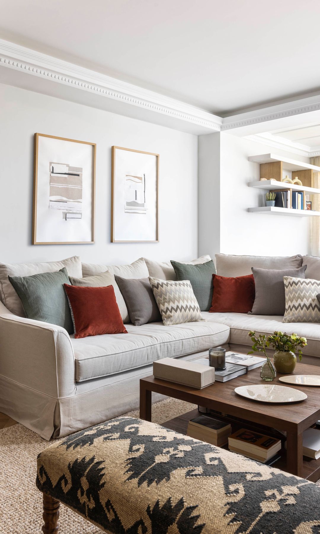 Salón con sofá beige, cojines de distintos colores, cuadros en la pared del sofá, mesa de centro de madera 