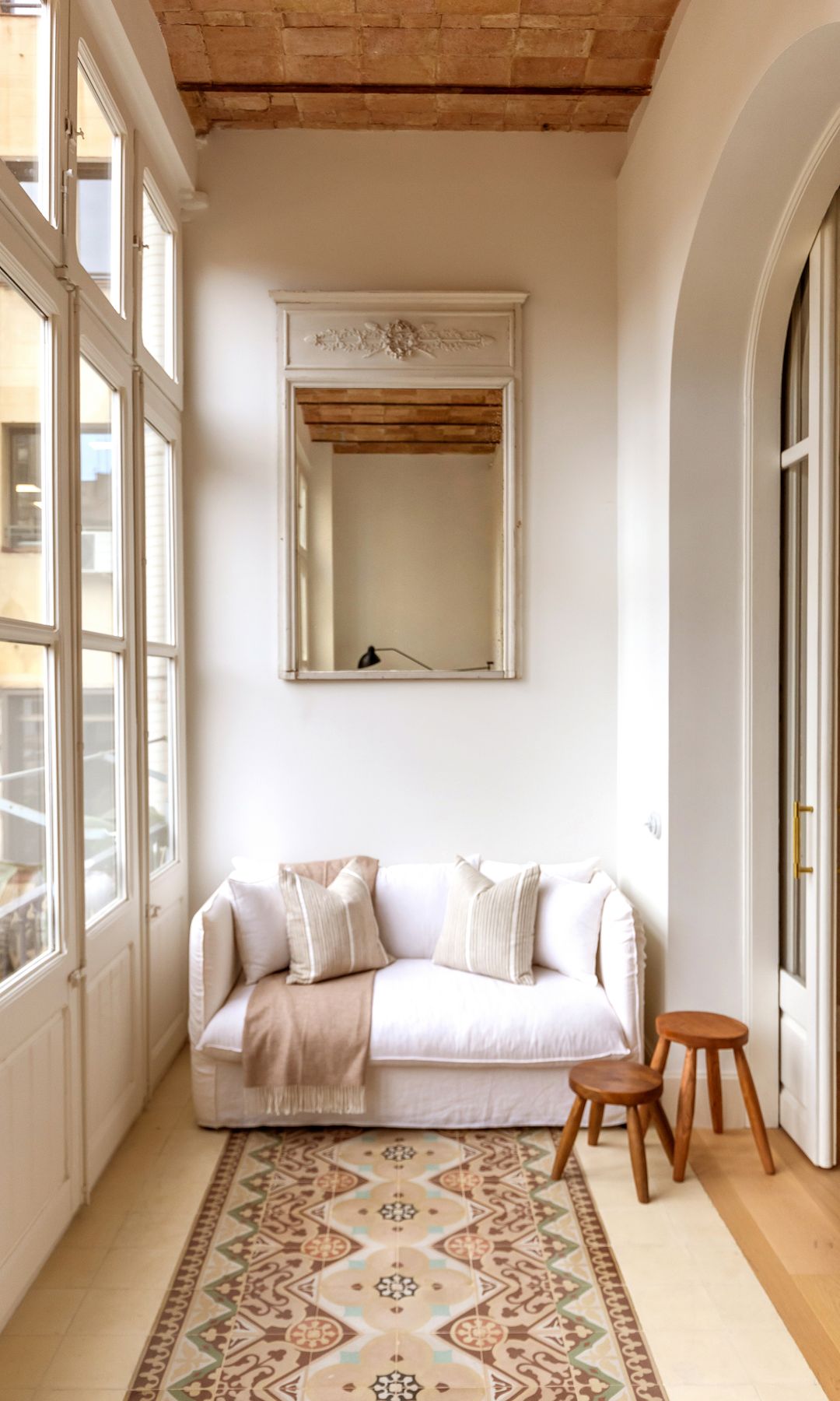 Galería con ventanas de madera blanca, suelo hidráulico, bóvedas catalana en el techo, sofá blanco pequeño