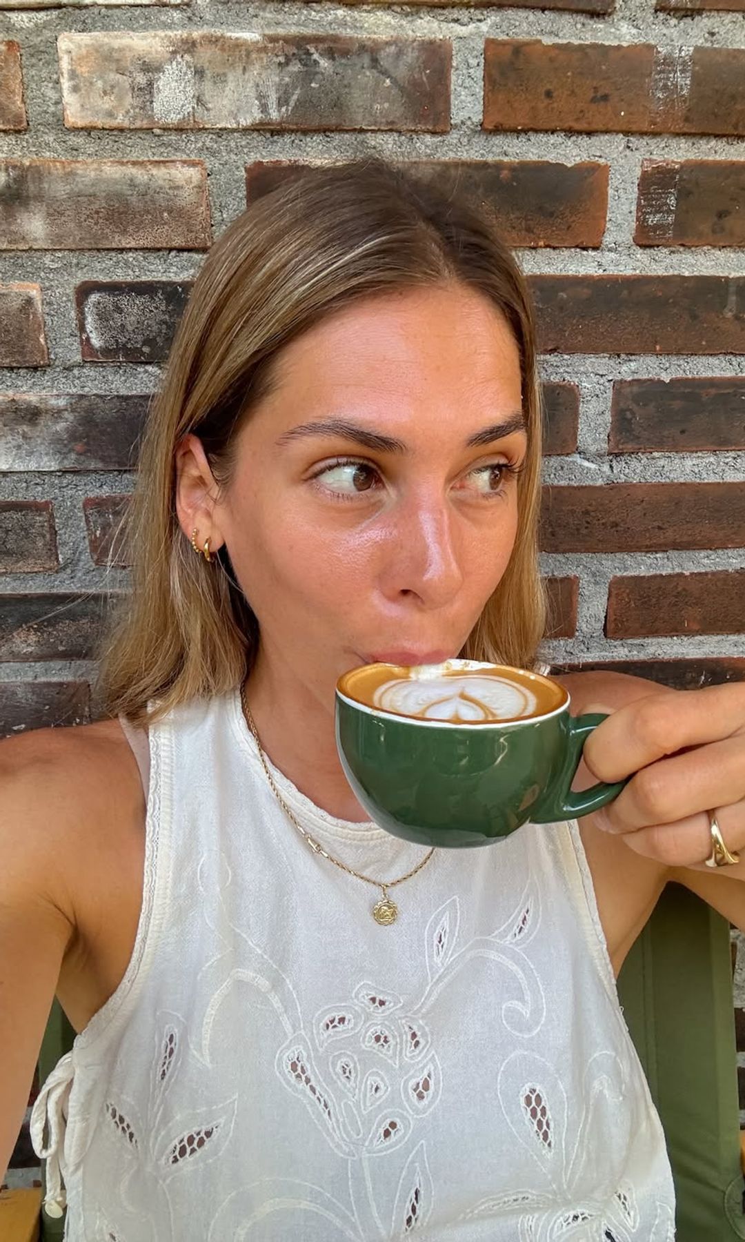 Mujer tomando café en una taza verde frente a un muro de ladrillo