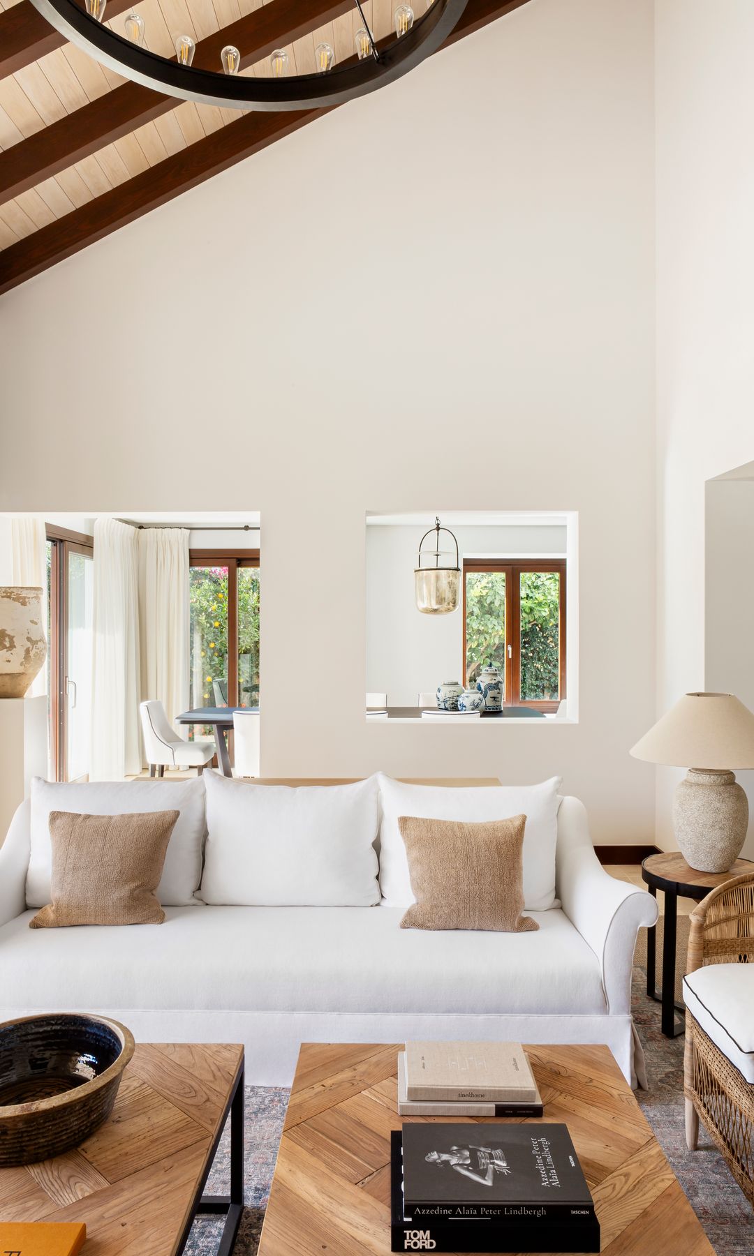Salón con sofá blanco, techo con vigas de madera, mesas de madera, lámpara de sobremesa, cojines beiges 