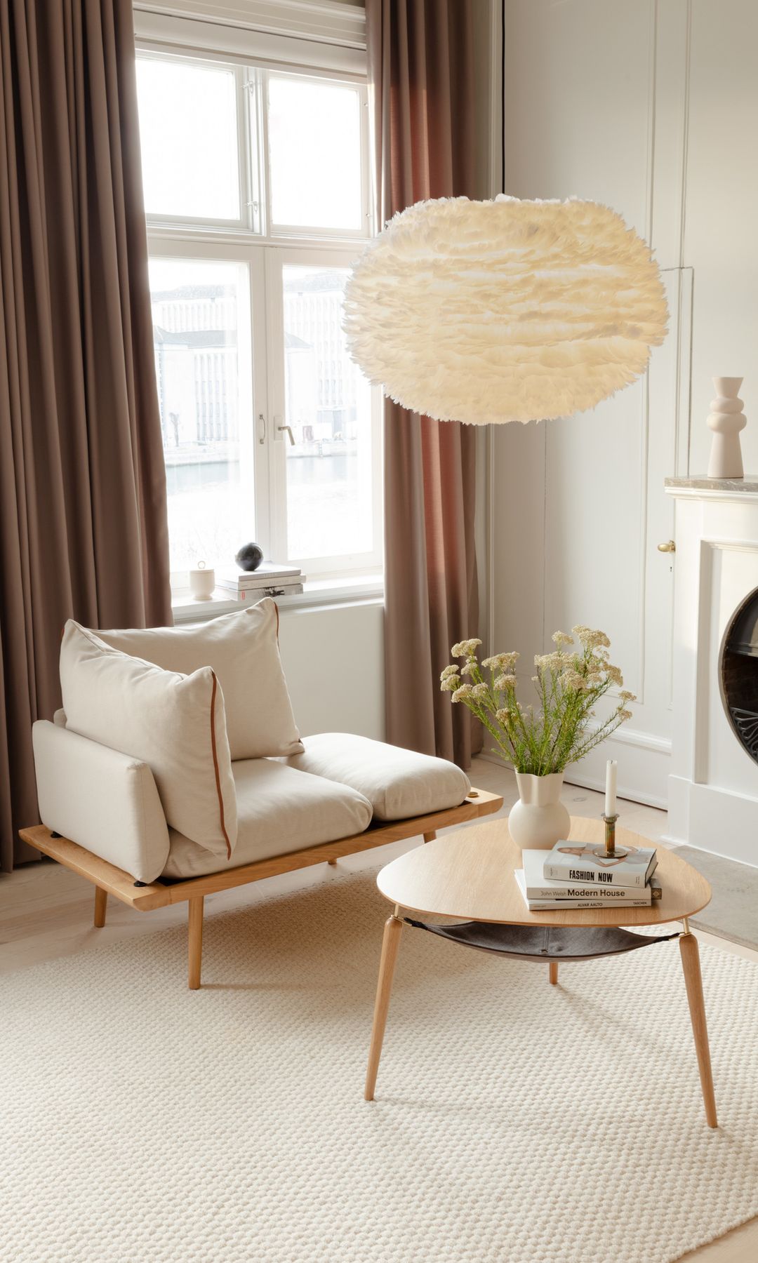 Salón con chimenea, sofá de madera, lámpara de techo de plumas, alfombra, mesa de centro con bandeja, cortinas marrones 