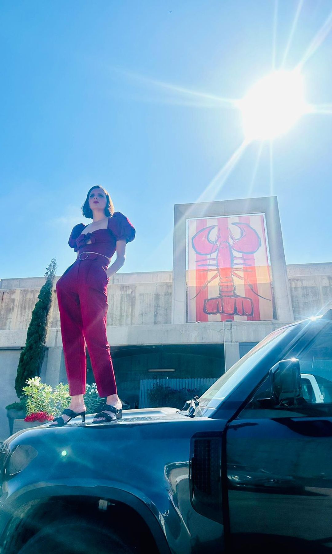 Macarena Gómez posando en el capó de un coche delante de una de las langostas de Aldo Comas