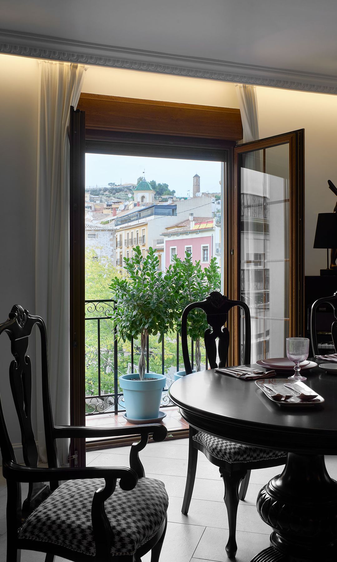 Comedor clásico con muebles negros, sillas tapizadas y de madera, salida al balcón 