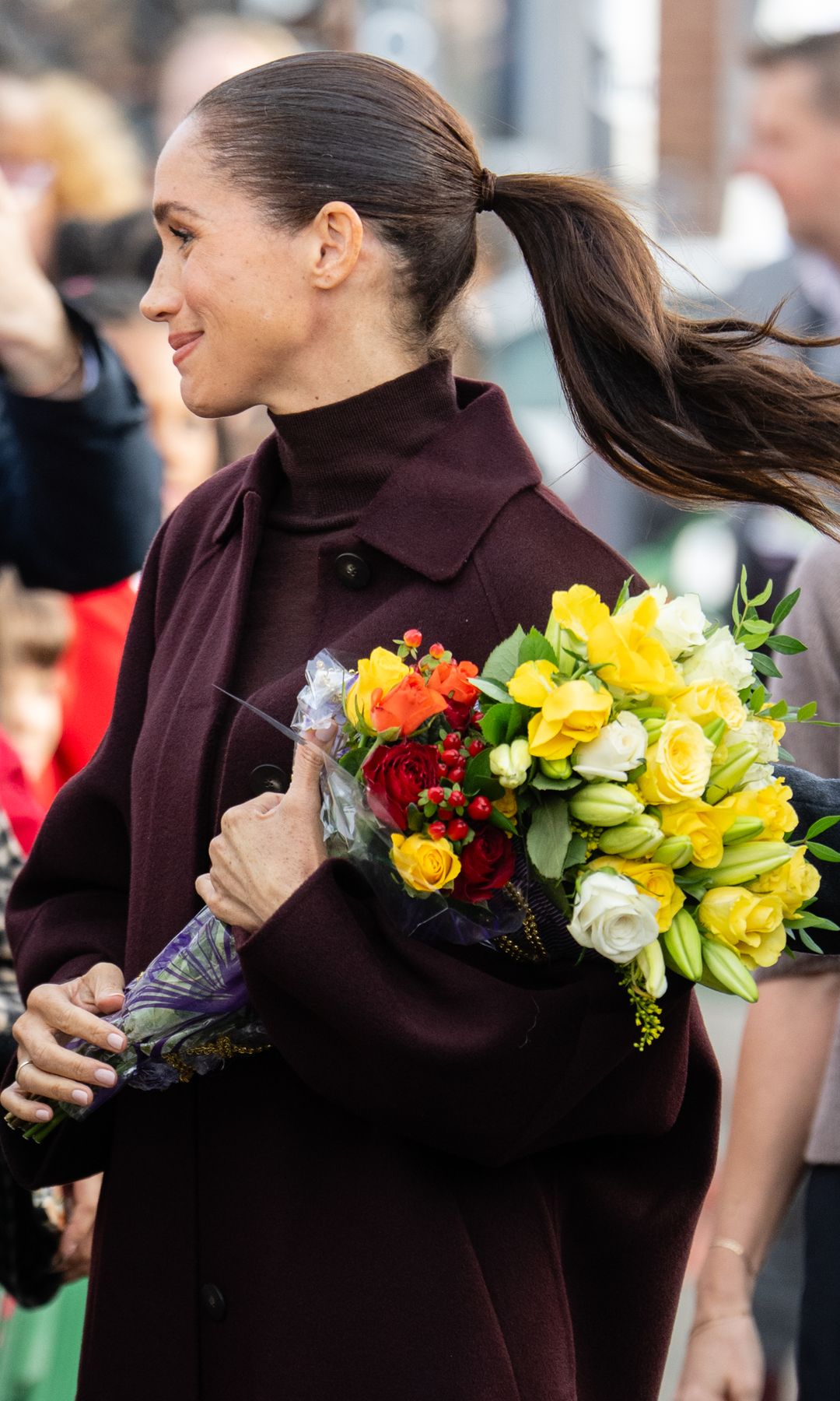 Meghan Markle con estilismo granate, ramo de flores en la mano en las calles de Nottingham