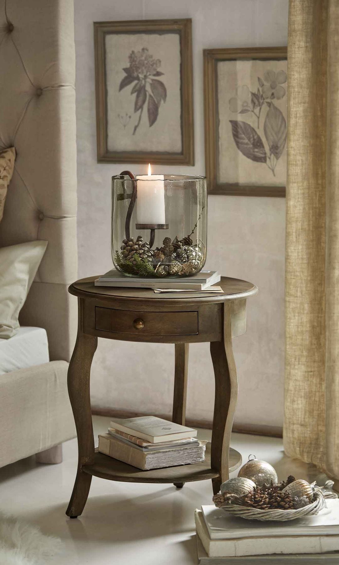 Dormitorio, cabecero tapizado, decoración Navidad con velas y jarrón de cristal con piñas, mesa auxiliar de estilo clásico con libros, bolas de Navidad en una bandeja, cortinas beige